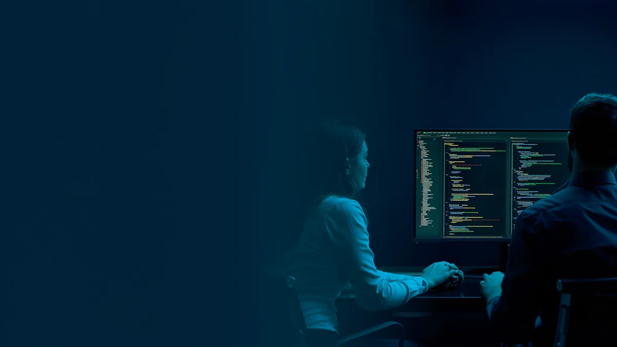 Deux développeurs devant un écran affichant du code, dans un bureau sombre